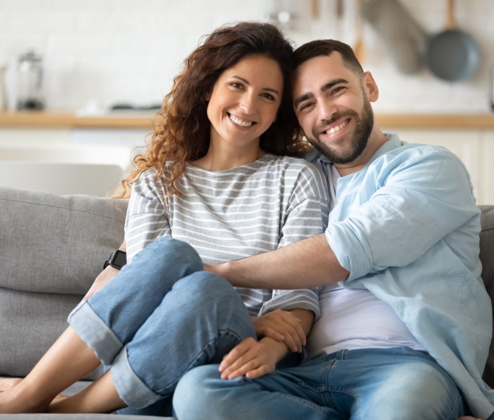 Portrait of young 35s just married couple in love posing photo shooting seated on couch in modern studio apartments, concept of capture happy moment, harmonic relationships, care and sincere feelings